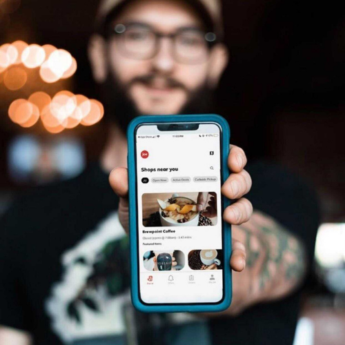 Man holding out iphone with joe coffee app "shops near me" page